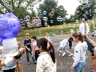 Kinder spielen auf dem Schulhof Limbo. um sie herum fliegen viele Seifenblasen