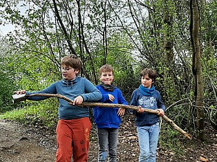 Drei Jungen im Wald. Sie halten einen großen Ast in der Hand