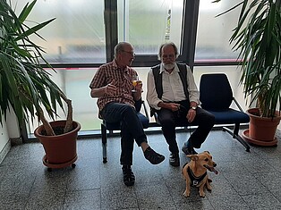 Zwei männliche Besucher sitzen auf der Band vor dem Trausaal und unterhalten sich