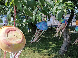 Von den Kindern gebastelte Quallen aus bemalten Schalen und Pfeiffenreinigern hängen an den Ästen eines Baumes.