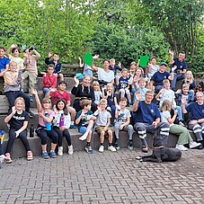 Gruppenfoto der Kinder mit mehreren Hundeführern. Alle winken in die Kamera