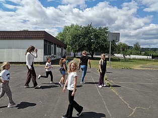 Kinder stehen in Kleingruppen zusammen mit den Betreuern auf einem Schulhof