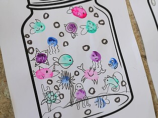 Auf einem Papier sind die Umrisse eines Schraubglases gedruckt. Im Inneren wurde mit Fingerfarbe und Fingerabdrücken Fische, Quallen und andere Tiere erstellt, die dann mit einem Stift vervollständigt wurden.