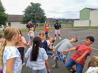 Kinder spielen auf dem Schulhof Limbo. um sie herum fliegen viele Seifenblasen