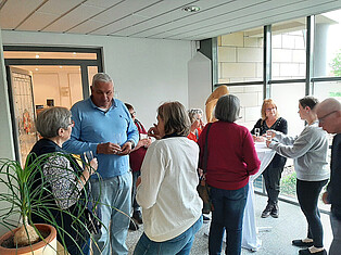 Besucherinnen und Besucher stehen im Vorraum beim Sektempfang und unterhalten sich in Kleingruppen.