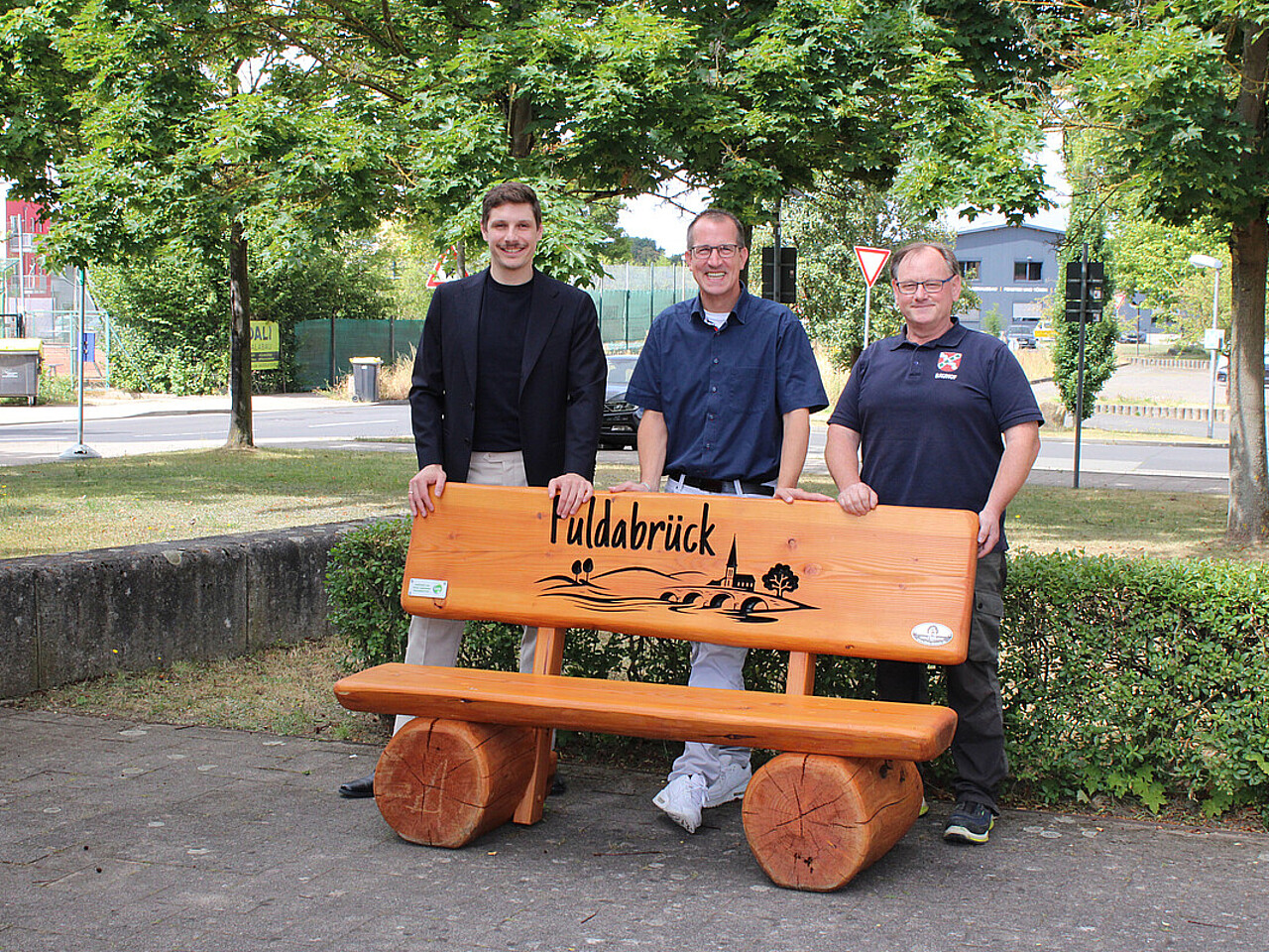 Am Tag der Übergabe der Sitzbank: v.l. Christof Mühling (EAM), Andreas Damm (Bürgermeister), Jörg Walter (Bauhofsleiter) stehen hinter der neuen Holzbank vor dem Rathaus