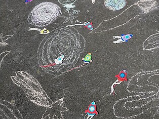 Mit Kreide gemalte Raumschiffe, Planeten und Sterne auf dem Schulhof