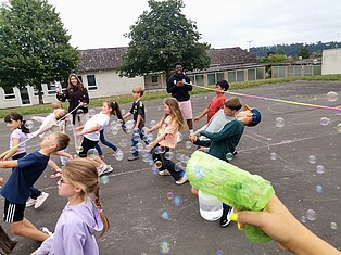 Kinder spielen auf dem Schulhof Limbo. um sie herum fliegen viele Seifenblasen