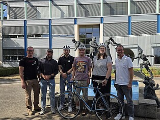 Andreas Hofmann (1. Beigeordneter), Jonas Döbel (Klimaschutzmanager), die Gewinnerinnen und Gewinner Lucian Altmann, Nils Rehwald u. Lea-Aileen Sirsch, sowie Andreas Damm (Bürgermeister) stehen vor dem Brunnen des Rathauses in Fuldabrück. Vor ihnen steht ein Fahrrad. Die drei Gewinner haben ihren neu gewonnenen Helm auf.
