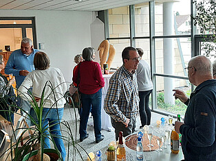 Die Besucherinnen und Besucher stehen im Vorraum beim Sektempfang und Unterhalten sich in Kleingruppen.