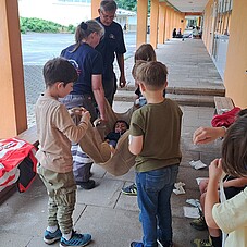 Foto wie mehrere Kinder ein Kind in einer Tragedecke tragen