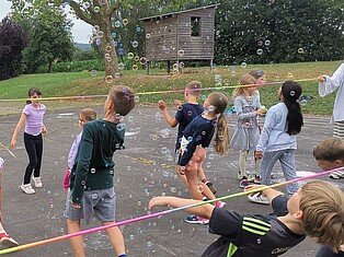 Kinder spielen auf dem Schulhof Limbo. um sie herum fliegen viele Seifenblasen