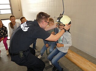 Ein Kind bekommt einen Feuewehrhelm aufgesetzt