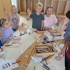 Foto einiger Kinder beim basteln, winkend in die Kamera