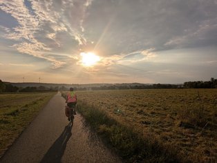 Ein Mann auf einem Fahrrad fährt auf einem Radweg in Richtung des Sonnenuntergangs