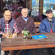 Foto einiger Teilnehmer bei einem Getränk. Sie sitzen auf einer Holzganitur
