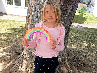 Ein Kind steht mit einem selbst gebastelten Regenbogen vor einem Baum