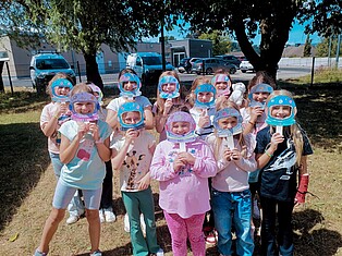 Einige Kinder stehen auf einer Wiese und halten sich ihre selbst gebastelten Astronautenhelme vor ihr Gesicht.