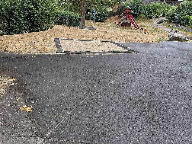 Eine ssphaltierte Fläche auf dem Spielplatz am Pappelweg vor einem Sandkasten 