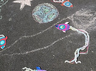 Mit Kreide gemalte Raumschiffe, Planeten und Sterne auf dem Schulhof
