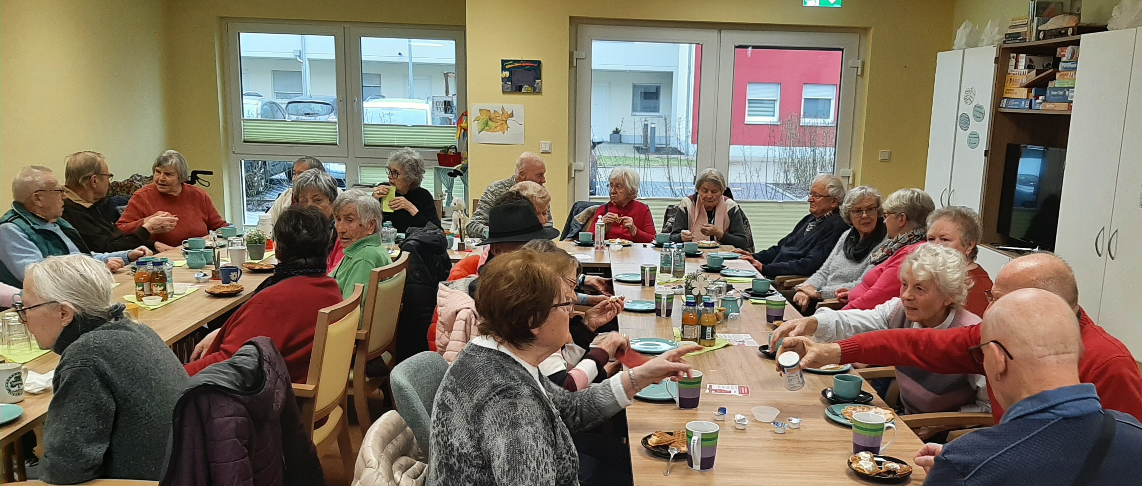 Senioren sitzen am Tisch und essen/trinken, unterhalten sich