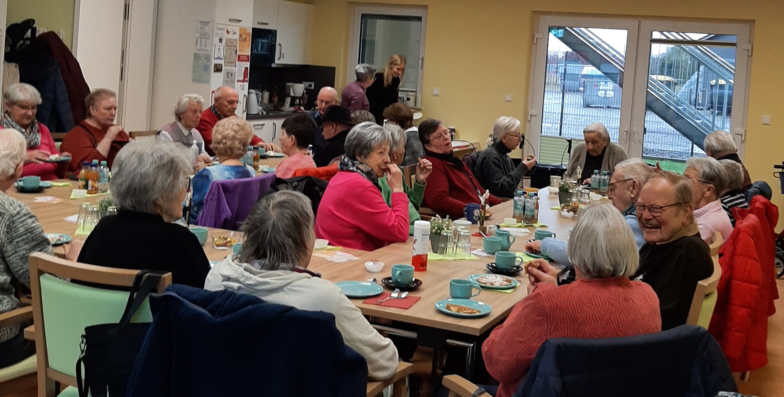 Senioren sitzen am Tisch und essen/trinken, unterhalten sich