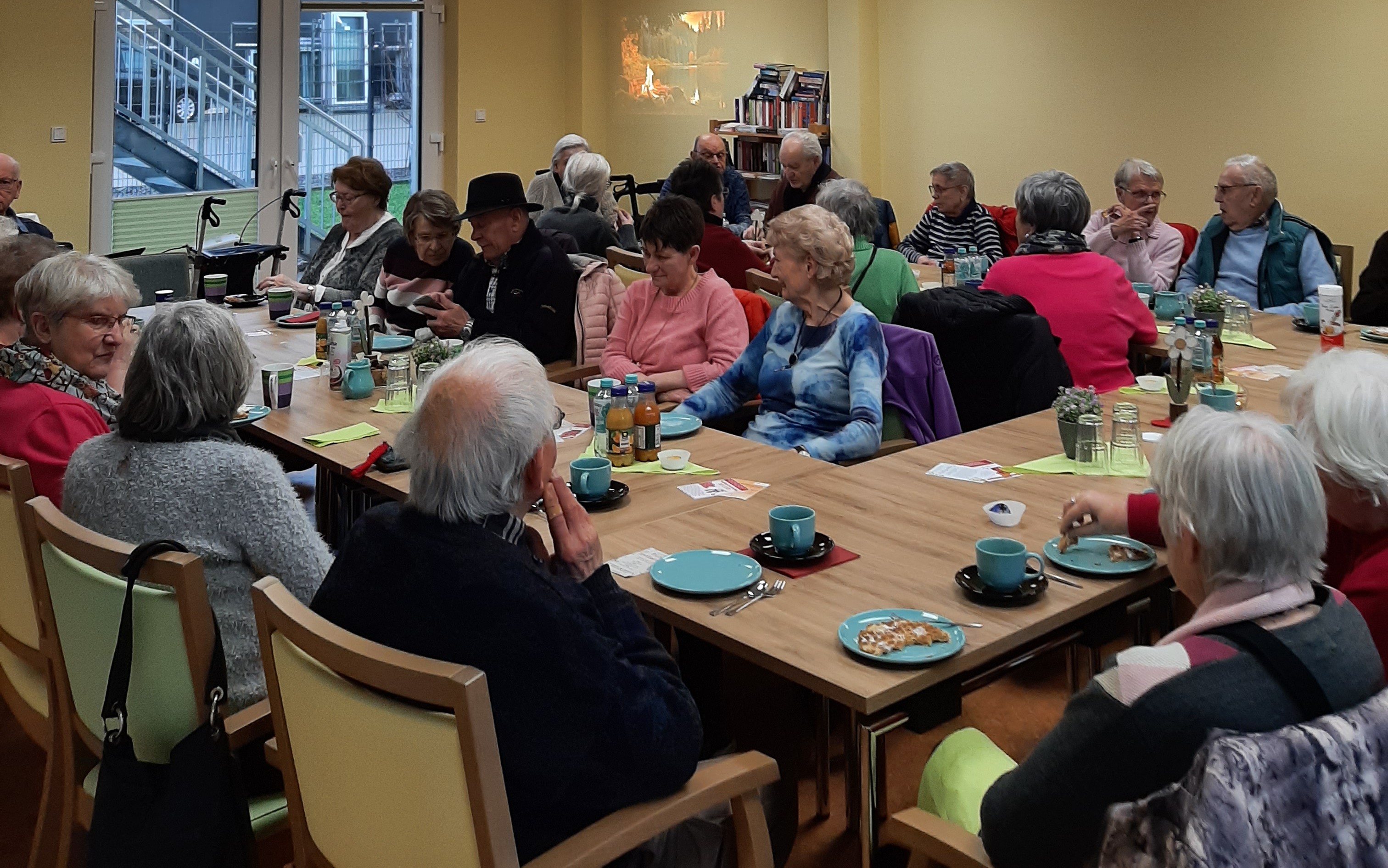 Senioren sitzen am Tisch und essen/trinken, unterhalten sich