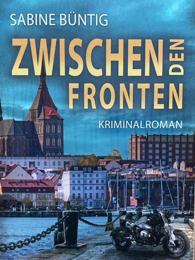 Buchcover "Zwischen den Fronten" von Sabine Büntig, Ein Motorrad steht an einer Hafenkante am Wasser, im Hintergrund sind kleine Segelboote und eine Stadt zu sehen.
